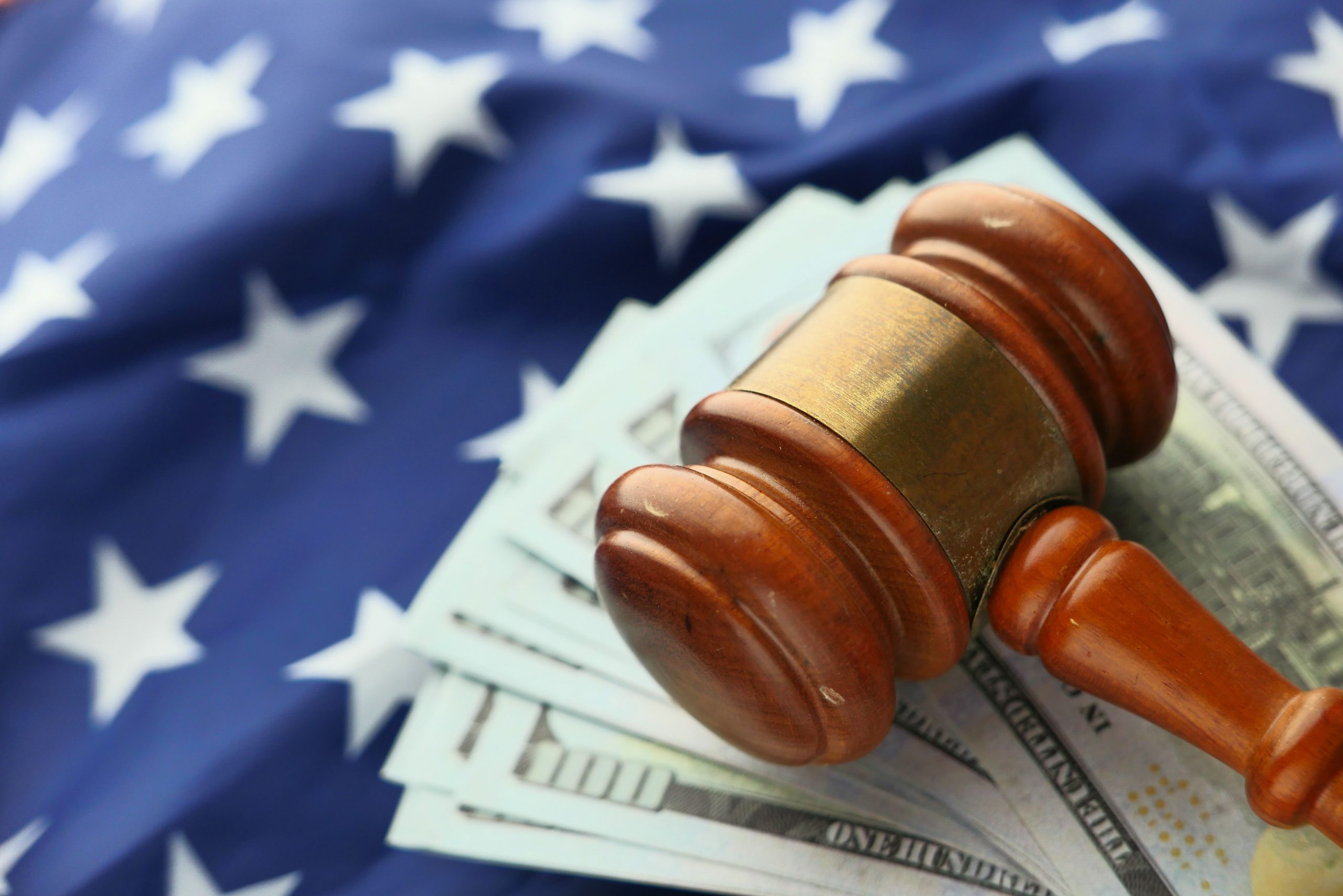 Close-up of a gavel resting on US dollar bills with an American flag backdrop, symbolizing the intersection of litigation and finance