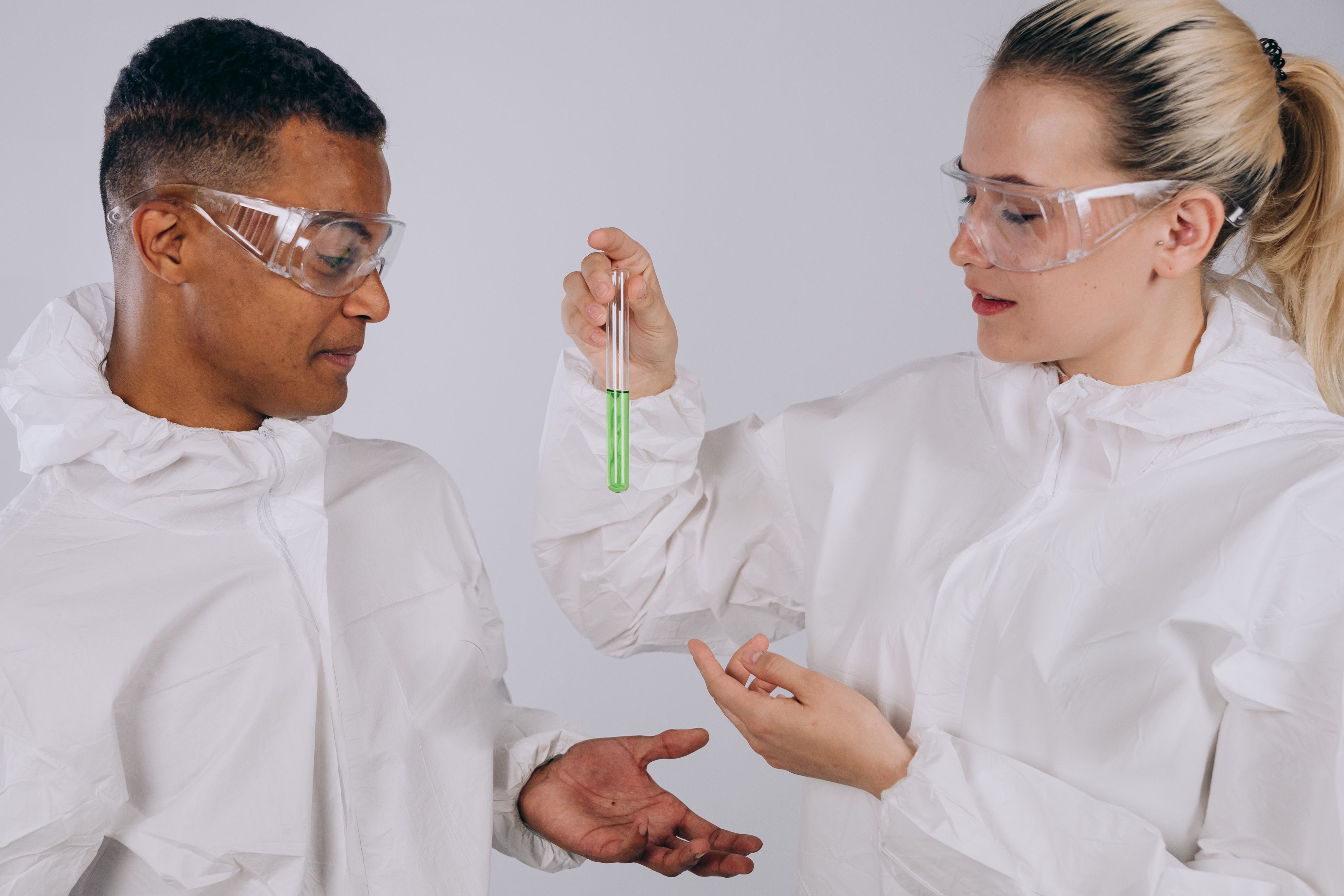 Two scientists in protective gear conducting an experiment with a green liquid in a test tube